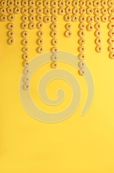 healthy corn flakes for breakfast in the form of pink and yellow rings in a transparent glass on a bright yellow background