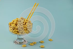 healthy corn flakes for breakfast in the form of yellow rings in a transparent glass on a bright yellow background