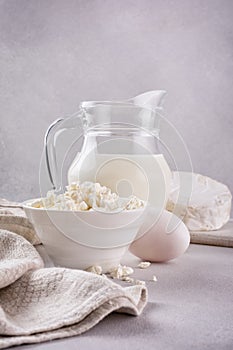 Healthy cottage cheese in a white bowl with a glass milk jug, eggs and camembert cheese