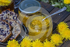 Healthy dandelion flower sweet jam in a glass jar on the wooden table with cherry muffin in the spring garden, closeup
