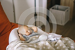 Healthy daytime sleep for the newborn. The baby is sleeping in the orthopedic Baby Cocoon on the bed in the room