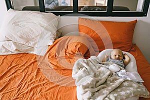 Healthy daytime sleep for the newborn. A child sleeps in the orthopedic Baby Cocoon on a larger bed in the parents room