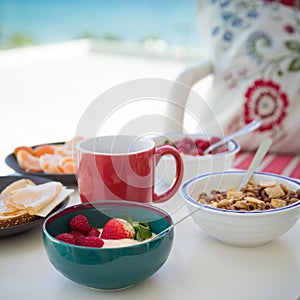 Healthy and delicious breakfast on the balcony with beautiful ocean view. Yogurt with fruit and organic berries, cereal and cheese