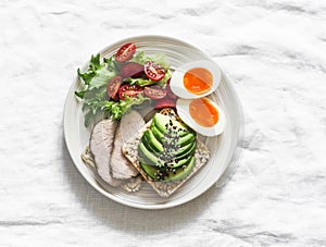 Healthy delicious breakfast on a light background - sandwich with avocado and baked turkey, boiled egg, fresh vegetable salad