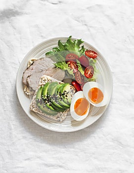 Healthy delicious breakfast on a light background - sandwich with avocado and baked turkey, boiled egg, fresh vegetable salad