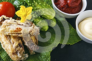 Healthy delicious chicken wings on a green cucumber leaves with fresh organic vegetables on a black background. Dietary rustic foo