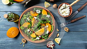 Healthy delicious winter salad with persimmon slices, mix of spinach, nuts, goat cheese, pomegranate, pumpkin seeds. Healthy