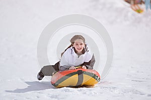 Healthy delightful little girl in ski suit riding on tube during snow tubing leisure activity on winter mountain alpine resort