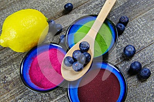 Healthy detox diet concept: bowls with brown aronia powder, green moringa, red beetroot and citrus fruit with blueberries on wood