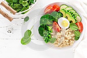 Healthy detox dish with egg, avocado, quinoa, spinach, fresh tomato, green peas and broccoli on white wooden background