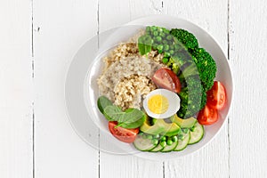 Healthy detox dish with egg, avocado, quinoa, spinach, fresh tomato, green peas and broccoli on white wooden background