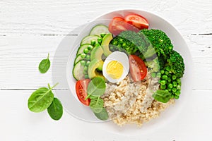 Healthy detox dish with egg, avocado, quinoa, spinach, fresh tomato, green peas and broccoli on white wooden background