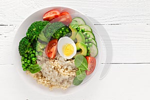 Healthy detox dish with egg, avocado, quinoa, spinach, fresh tomato, green peas and broccoli on white wooden background