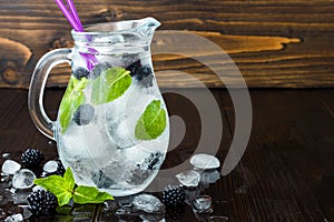 Healthy detox flavored water with blackberry and mint. Cold refreshing berry drink with ice on dark wooden table. Copy space backg