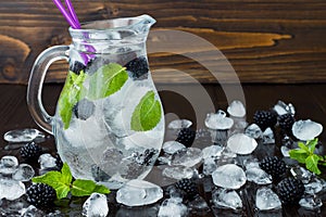 Healthy detox flavored water with blackberry and mint. Cold refreshing berry drink with ice on dark wooden table. Copy space backg