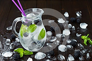 Healthy detox flavored water with blackberry and mint. Cold refreshing berry drink with ice on dark wooden table. Copy space backg