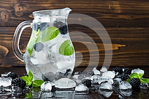 Healthy detox flavored water with blackberry and mint. Cold refreshing berry drink with ice on dark wooden table. Copy space backg