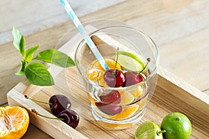 Healthy detox water, glass of cherry, orange and lime on wooden tray