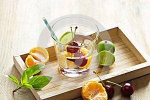 Healthy detox water, glass of cherry, orange and lime on wooden tray