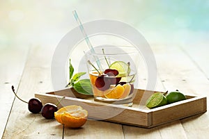 Healthy detox water, glass of cherry, orange and lime on wooden tray