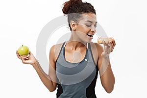 Healthy and diet concept - Beautiful sporty African American make a decision between donut and green apple. Isolated on
