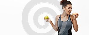 Healthy and diet concept - Beautiful sporty African American make a decision between donut and green apple. Isolated on