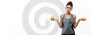 Healthy and diet concept - Beautiful sporty African American make a decision between donut and green apple. Isolated on