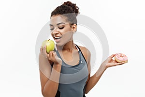 Healthy and diet concept - Beautiful sporty African American make a decision between donut and green apple. Isolated on