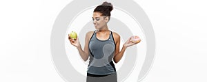 Healthy and diet concept - Beautiful sporty African American make a decision between donut and green apple. Isolated on