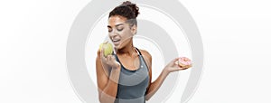 Healthy and diet concept - Beautiful sporty African American make a decision between donut and green apple. Isolated on