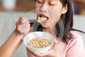 Healthy diet concept. Korean lady eating cereals with yoghurt, having nutritious breakfast at home, closeup