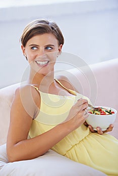 Healthy diet for her babys benefit. A relaxed pregnant woman enjoying a healthy salad while sitting on the couch.