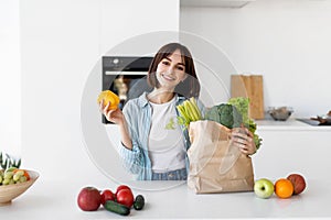 Healthy diet and lifestyle. Happy young lady unpacking paper bag with fresh organic vegetables, greens and fruits