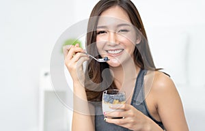 Healthy Diet And Nutrition. Portrait of happy beautiful young Asian woman eating natural yogurt at home and looking at camera.