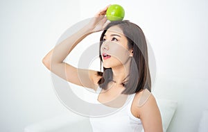 Healthy Diet And Nutrition. Protrait of a beautiful Asian woman relaxing sitting on sofa holding a green apple on her head.Weight