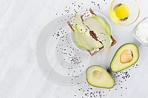 Healthy dietary breakfast of crisps rye flat toast with fresh avocado slices, olive oil, black sesame seeds, cream cheese on white