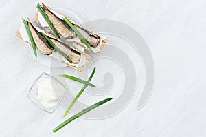 Healthy dietary breakfast of whole grain wheat crisps breads with anchovies, cream cheese, green onion sprout on white wood.