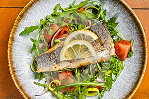 Healthy diner with sea bass fillet and vegetable salad, seabass fish. Orange background. Top view