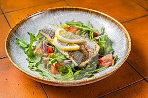 Healthy diner with sea bass fillet and vegetable salad, seabass fish. Orange background. Top view