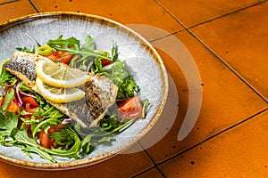 Healthy diner with sea bass fillet and vegetable salad, seabass fish. Orange background. Top view. Copy space