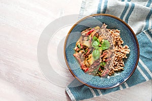 Healthy dish from wholemeal spelt pasta with vegetables in tomato sauce and basil garnish in a blue plate on a white wooden table