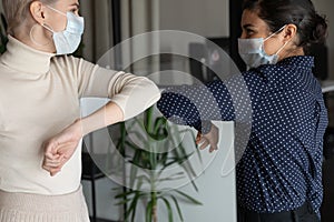 Healthy diverse colleagues in facial masks bumping elbows.