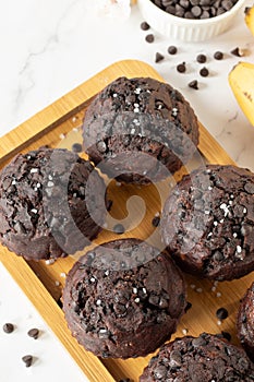 Healthy double chocolate chip muffins with bananas on a wooden plate, top view