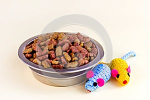 Healthy dry cat food. Brown crunchy organic kitty kibble pieces in a bowl for pet feed and mouse toys on light background.