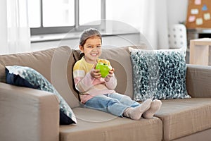 Happy little girl with apple sitting on sofa