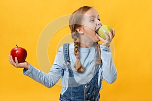 Healthy eating concept. A child bites an apple. Little girl on a yellow background