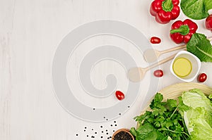 Healthy eating concept - fresh green salad, cherry tomatoes, paprika, spinach and olive oil on white wood board, top view.