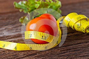 Healthy eating concept. Tomato with measure tape, Fork and vegetable with measure tape on wooden desk