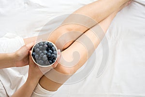 Healthy eating concept. Woman having blueberries in bed.
