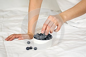 Healthy eating concept. Woman having blueberries in bed.